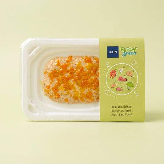 A packaged pet food product on a pale yellow background. The white plastic tray contains a rectangular piece of dog food topped with orange and yellow crumb pieces. Furry Green x Ixon